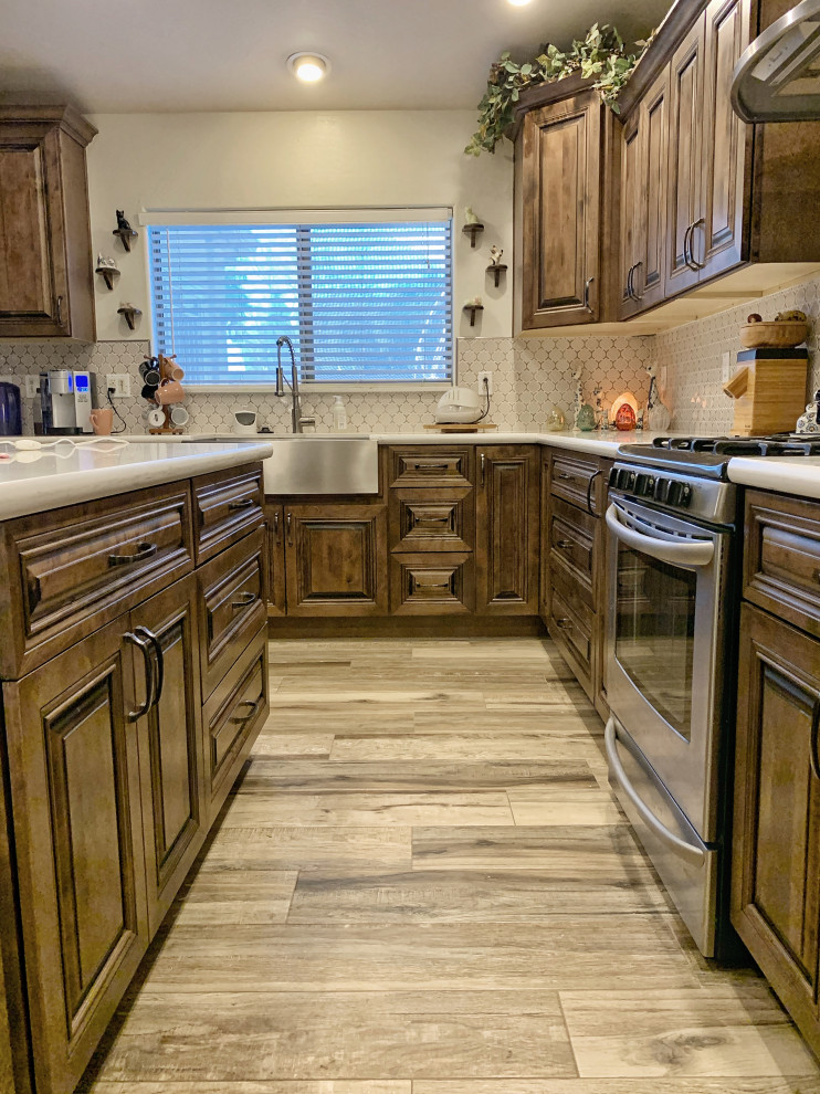 Photo of a mid-sized traditional l-shaped open plan kitchen in Phoenix with a farmhouse sink, raised-panel cabinets, distressed cabinets, quartz benchtops, white splashback, glass sheet splashback, stainless steel appliances, ceramic floors, with island, beige floor and white benchtop.