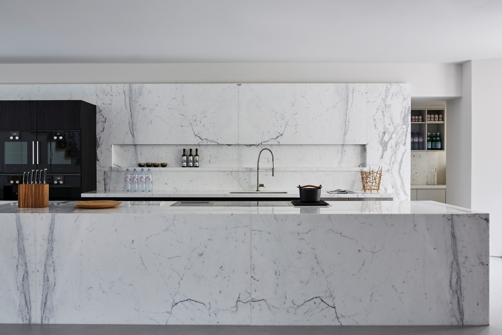 Photo of a large contemporary kitchen in London with marble benchtops, marble splashback, with island, an undermount sink and black appliances.