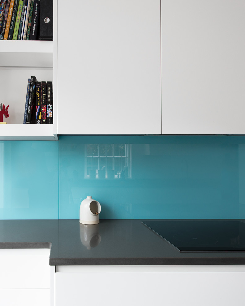 Mid-sized modern galley eat-in kitchen in London with a double-bowl sink, flat-panel cabinets, white cabinets, solid surface benchtops, blue splashback, glass sheet splashback, stainless steel appliances, porcelain floors and no island.