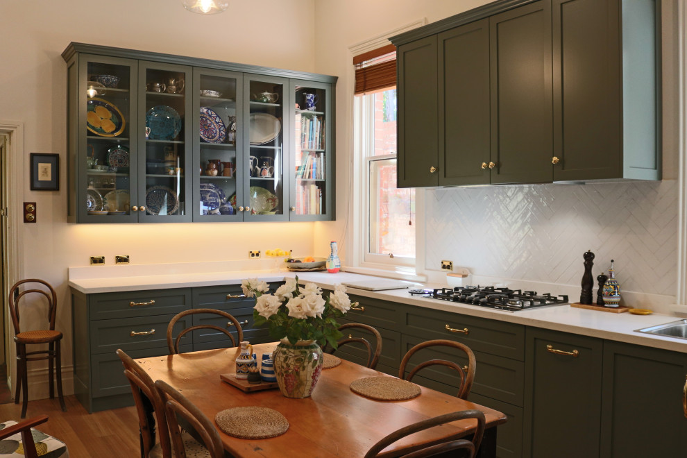 Victorian l-shaped eat-in kitchen with a double-bowl sink, shaker cabinets, green cabinets, quartz benchtops, white splashback, ceramic splashback, stainless steel appliances, light hardwood floors and white benchtop.
