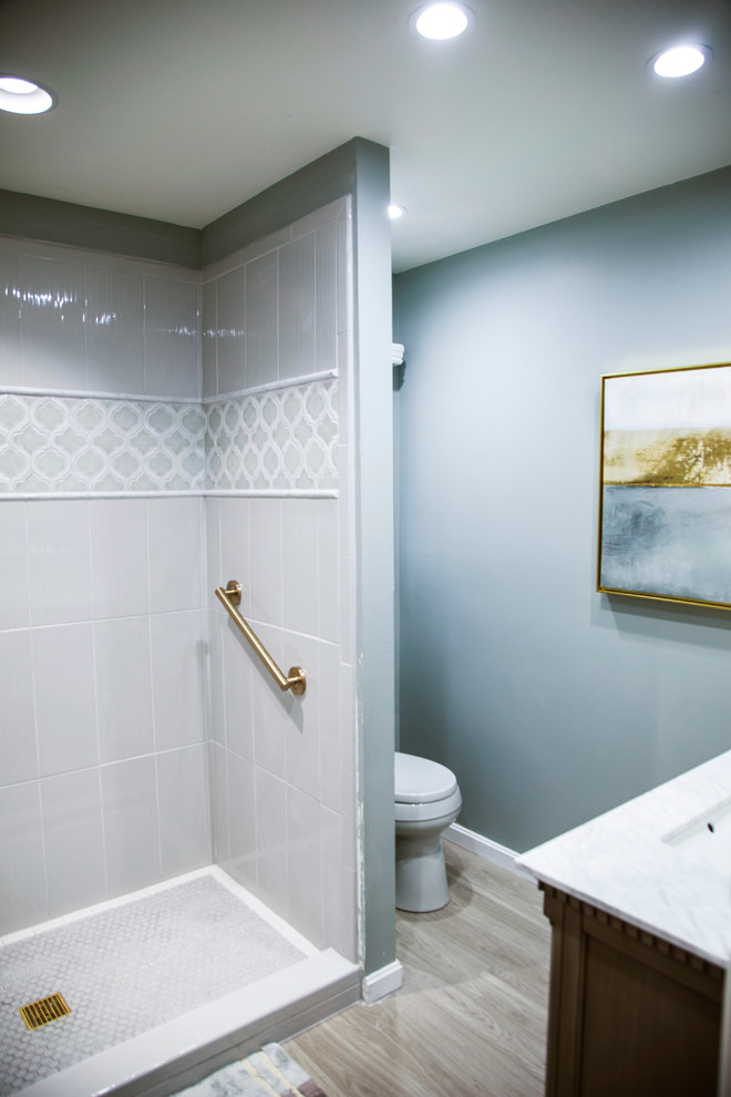 Inspiration for a small transitional 3/4 bathroom in Louisville with furniture-like cabinets, grey cabinets, an alcove shower, a two-piece toilet, gray tile, ceramic tile, grey walls, laminate floors, an integrated sink, marble benchtops, grey floor, a hinged shower door and white benchtops.