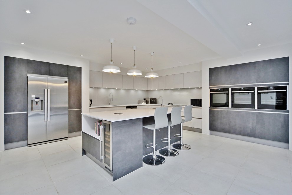 Inspiration for a large contemporary l-shaped open plan kitchen in Surrey with an undermount sink, flat-panel cabinets, grey cabinets, quartzite benchtops, metallic splashback, glass sheet splashback, stainless steel appliances, porcelain floors, with island, grey floor and white benchtop.