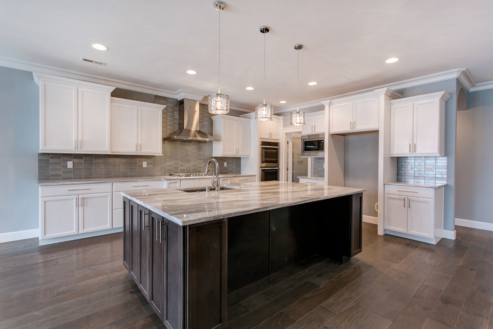 Large transitional l-shaped dark wood floor open concept kitchen photo in Seattle with an undermount sink, recessed-panel cabinets, white cabinets, granite countertops, gray backsplash, glass tile backsplash, stainless steel appliances and an island