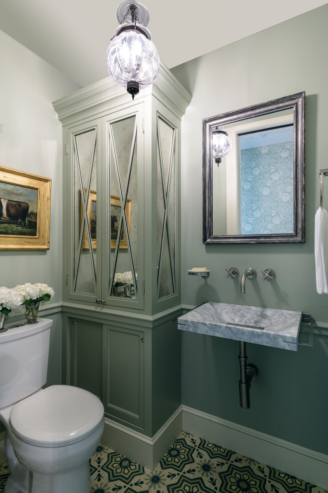 This is an example of a small traditional powder room in New York with recessed-panel cabinets, green cabinets, a two-piece toilet, green walls, cement tiles, a wall-mount sink, marble benchtops, beige floor and grey benchtops.
