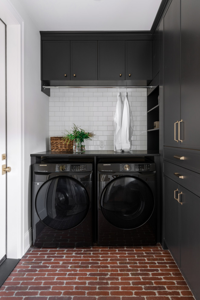 This is an example of a mid-sized transitional laundry room in Calgary with black cabinets, quartzite benchtops, white splashback, ceramic splashback, brick floors, a side-by-side washer and dryer and black benchtop.