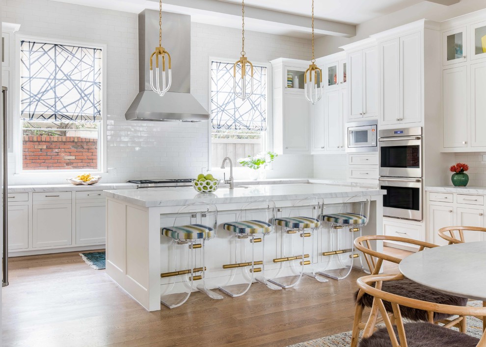 Beach style eat-in kitchen in Dallas with shaker cabinets, white cabinets, white splashback, subway tile splashback, stainless steel appliances, medium hardwood floors, with island and white benchtop.