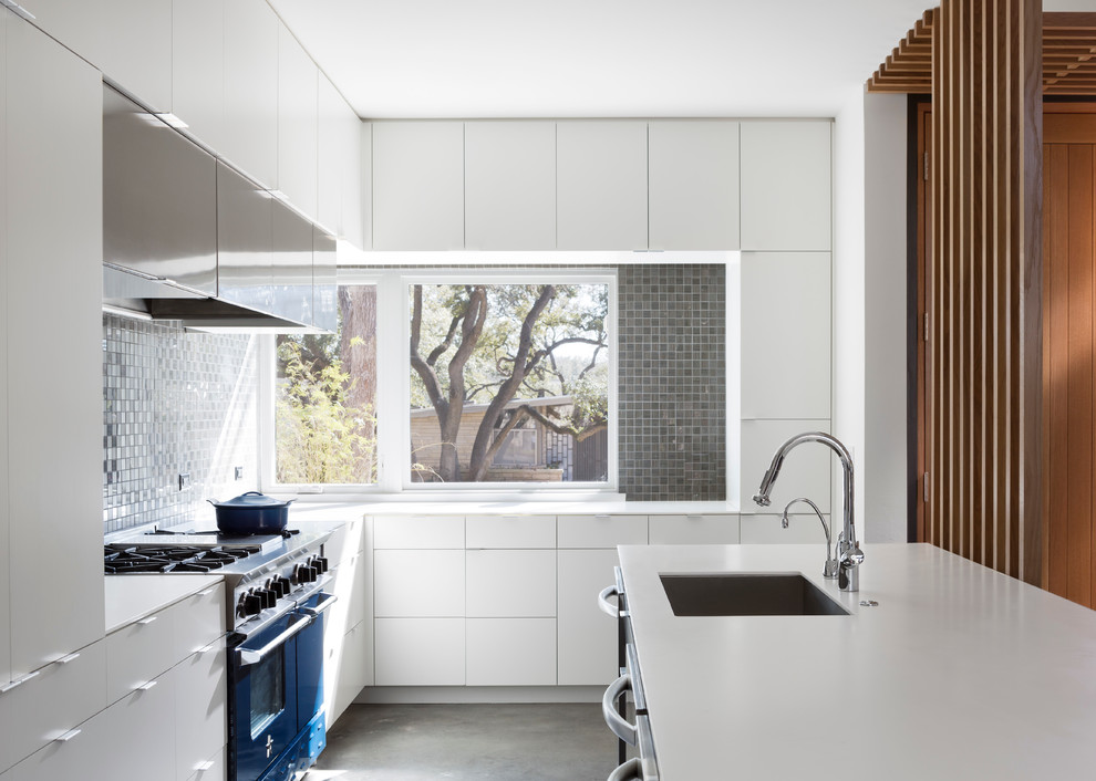 Photo of a midcentury kitchen in Austin with an undermount sink, flat-panel cabinets, white cabinets, metallic splashback, coloured appliances and concrete floors.