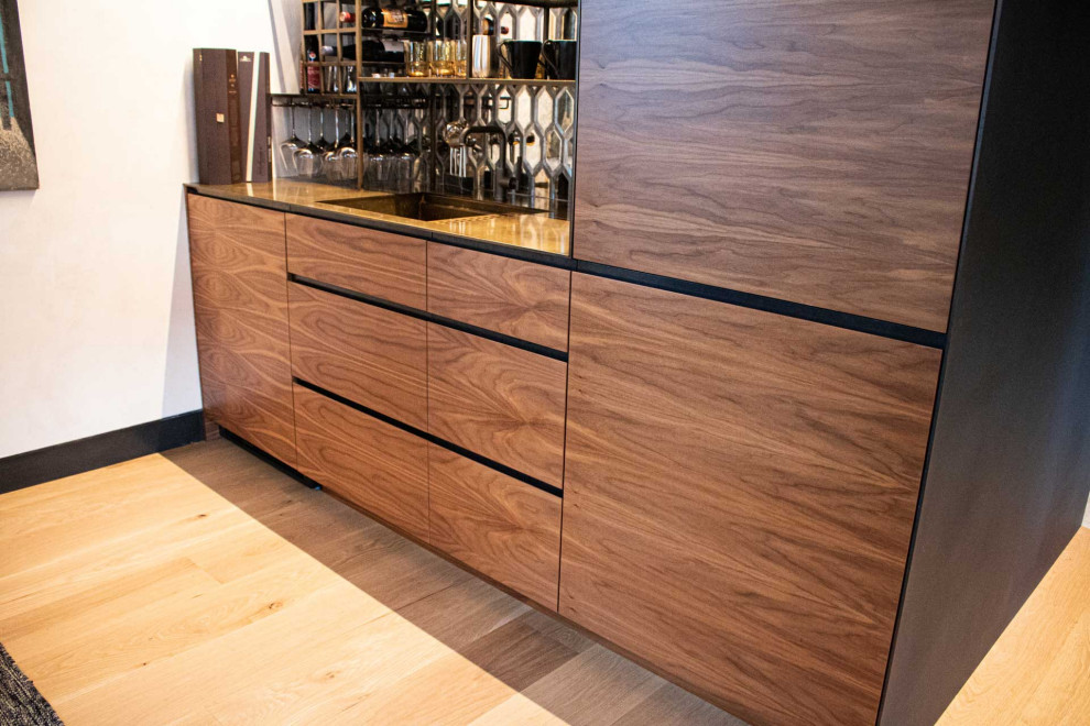 This is an example of a medium sized contemporary galley wet bar in Other with an integrated sink, flat-panel cabinets, medium wood cabinets, stainless steel worktops, glass sheet splashback, light hardwood flooring, brown floors and yellow worktops.