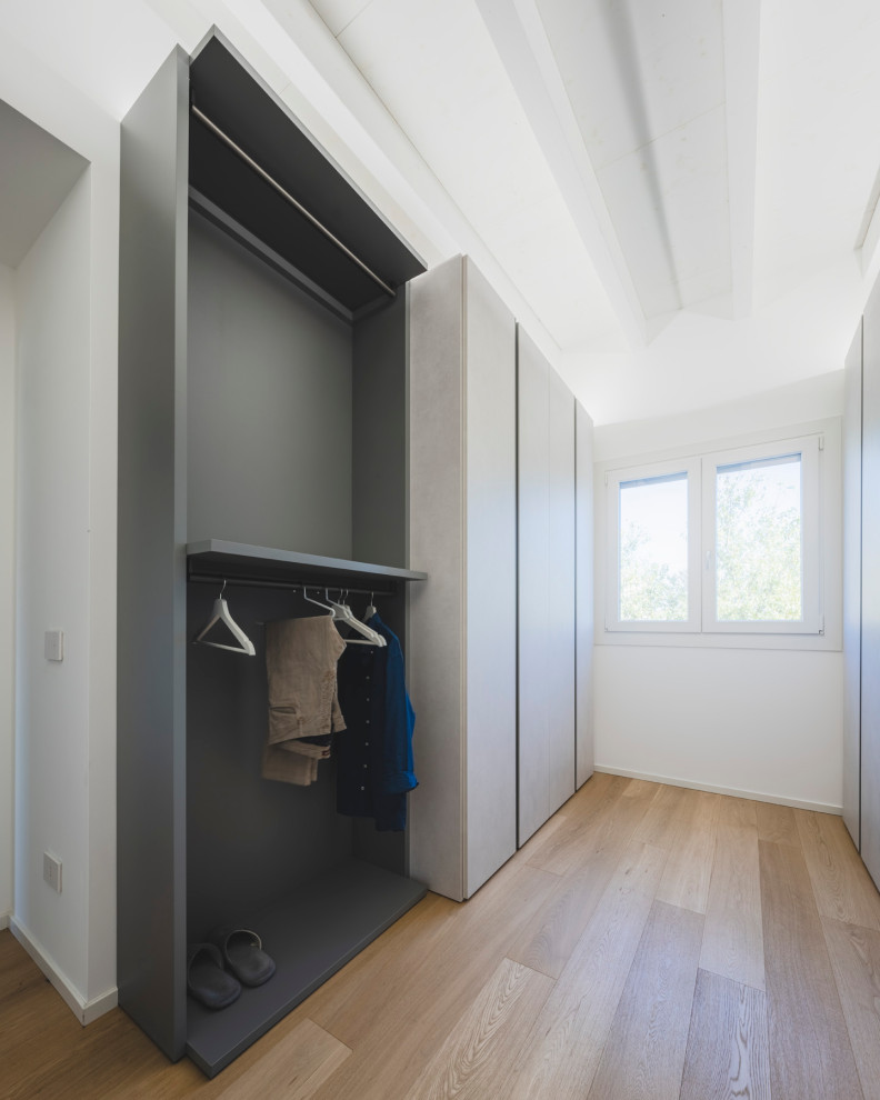 This is an example of a large scandinavian men's walk-in wardrobe in Milan with flat-panel cabinets, grey cabinets, light hardwood floors, beige floor and exposed beam.