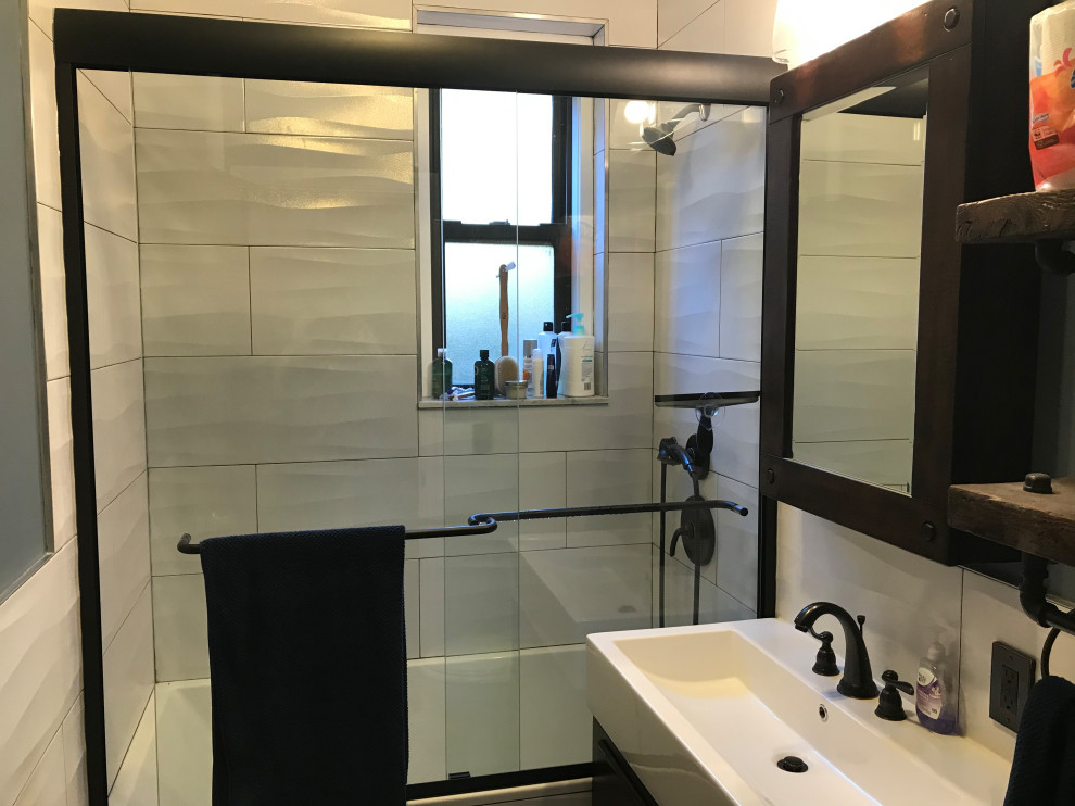 This is an example of a small modern 3/4 bathroom in New York with furniture-like cabinets, black cabinets, an alcove tub, a shower/bathtub combo, a two-piece toilet, white tile, porcelain tile, white walls, ceramic floors, a trough sink, solid surface benchtops, multi-coloured floor, a sliding shower screen and white benchtops.