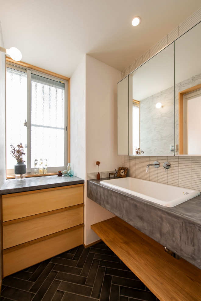Photo of a mid-sized asian powder room in Other with white tile, matchstick tile, ceramic floors, open cabinets, white walls, a drop-in sink, concrete benchtops, black floor and grey benchtops.