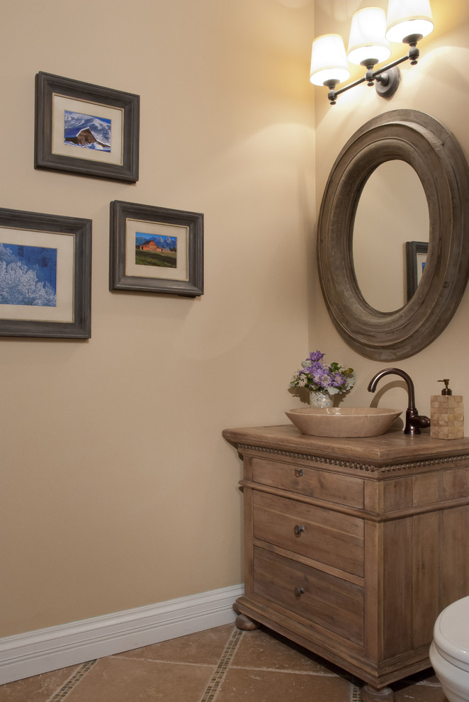 This is an example of a mid-sized transitional powder room in St Louis with furniture-like cabinets, medium wood cabinets, beige walls, terra-cotta floors, a vessel sink, wood benchtops and brown benchtops.