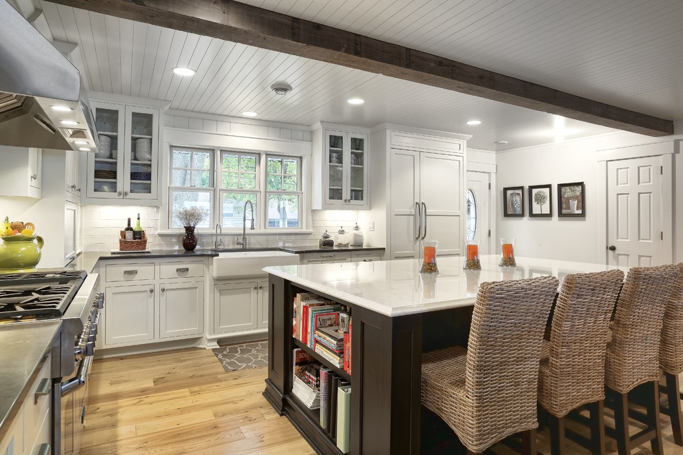 This is an example of a traditional l-shaped kitchen in Minneapolis with a farmhouse sink, flat-panel cabinets, white cabinets, white splashback and panelled appliances.