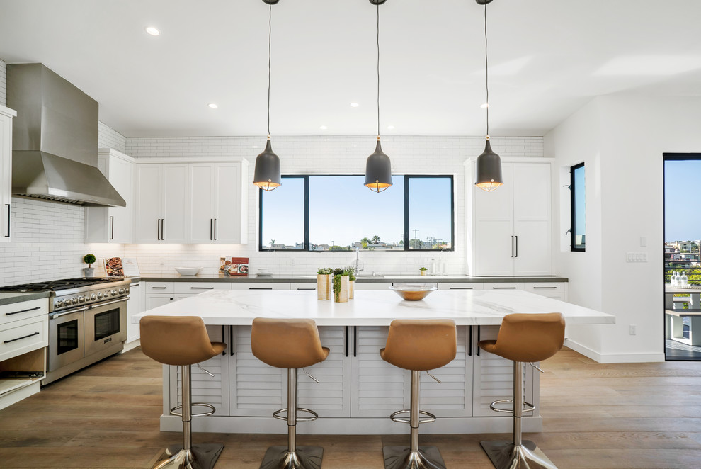 Inspiration for a transitional open plan kitchen in Los Angeles with an undermount sink, louvered cabinets, white cabinets, white splashback, subway tile splashback, stainless steel appliances, medium hardwood floors, with island, brown floor and white benchtop.