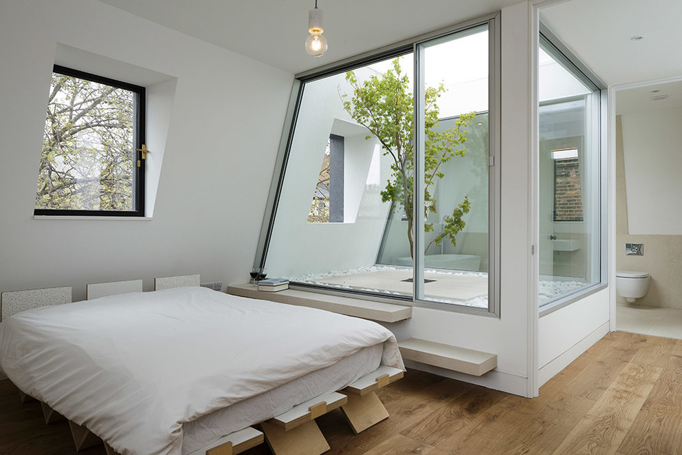 Mid-sized contemporary master bedroom in London with white walls and light hardwood floors.