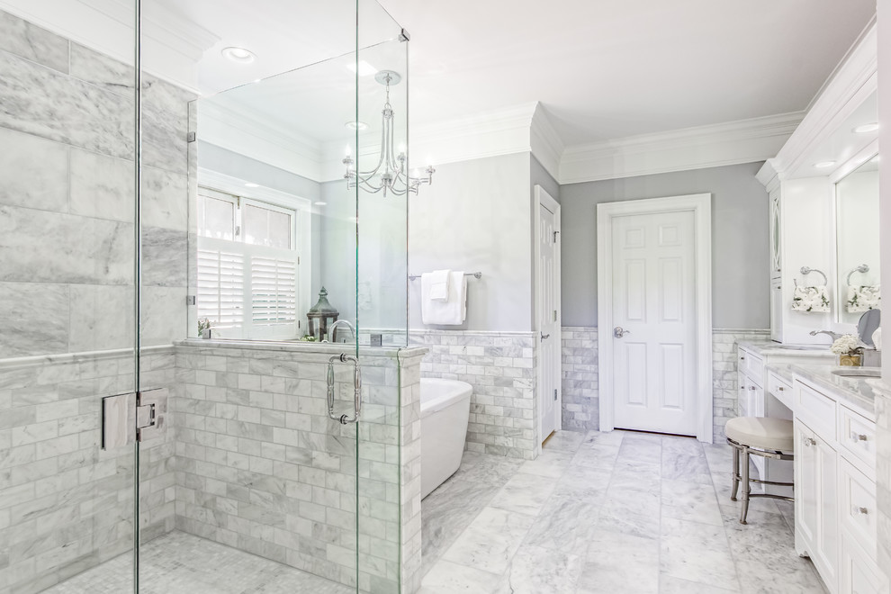 Photo of a large traditional master bathroom in Columbus with beaded inset cabinets, white cabinets, a freestanding tub, a curbless shower, gray tile, marble, grey walls, marble floors, an undermount sink, marble benchtops, grey floor, a hinged shower door and white benchtops.