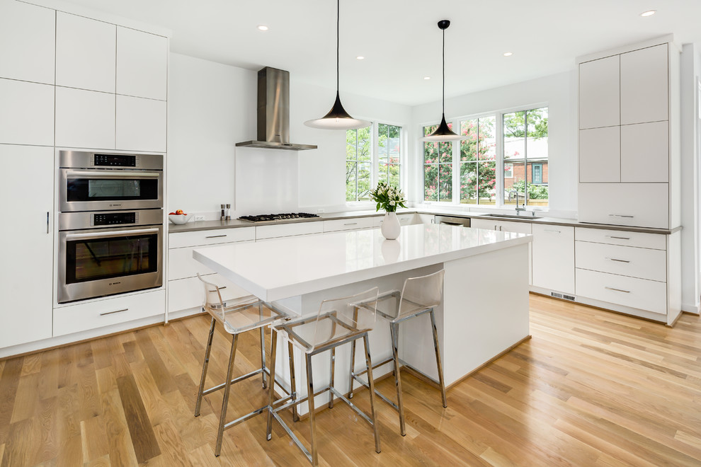 This is an example of a mid-sized modern l-shaped open plan kitchen in DC Metro with an undermount sink, flat-panel cabinets, white cabinets, quartzite benchtops, stainless steel appliances, light hardwood floors, with island and beige floor.