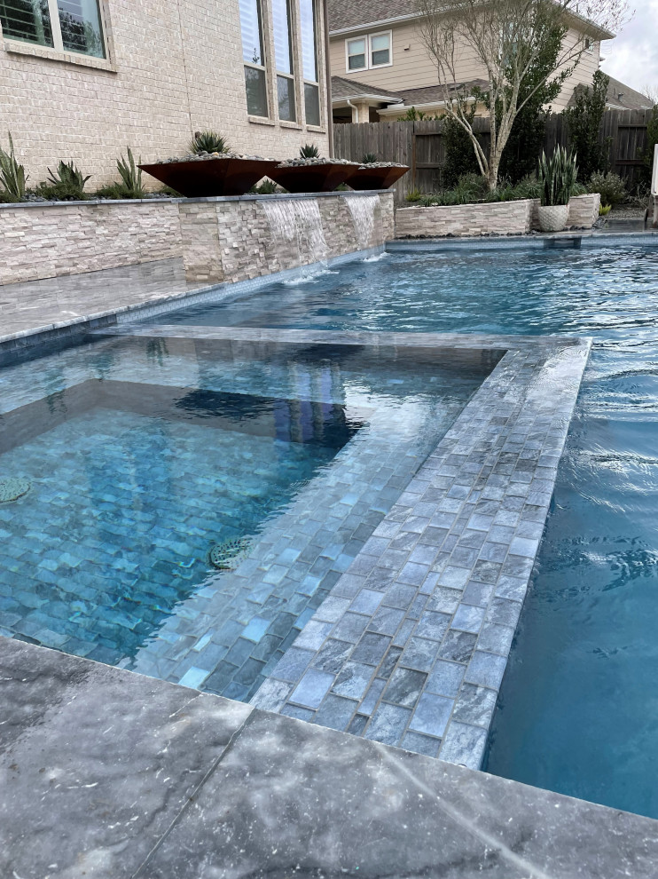 Exemple d'une grande piscine à débordement et latérale éclectique avec des pavés en pierre naturelle.