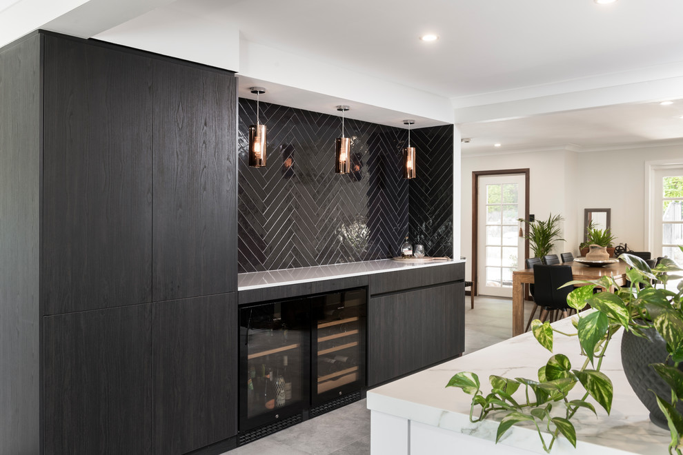 Photo of a mid-sized contemporary galley open plan kitchen in Perth with an undermount sink, flat-panel cabinets, dark wood cabinets, tile benchtops, black splashback, subway tile splashback, black appliances, cement tiles, with island, grey floor and white benchtop.