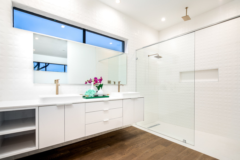 Design ideas for a mid-sized modern master bathroom in Dallas with flat-panel cabinets, white cabinets, an alcove shower, white tile, ceramic tile, white walls, medium hardwood floors, a vessel sink, engineered quartz benchtops, brown floor, white benchtops and an open shower.
