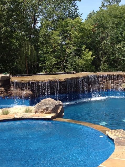 Inspiration for a large country backyard custom-shaped pool in Kansas City with a water feature and natural stone pavers.