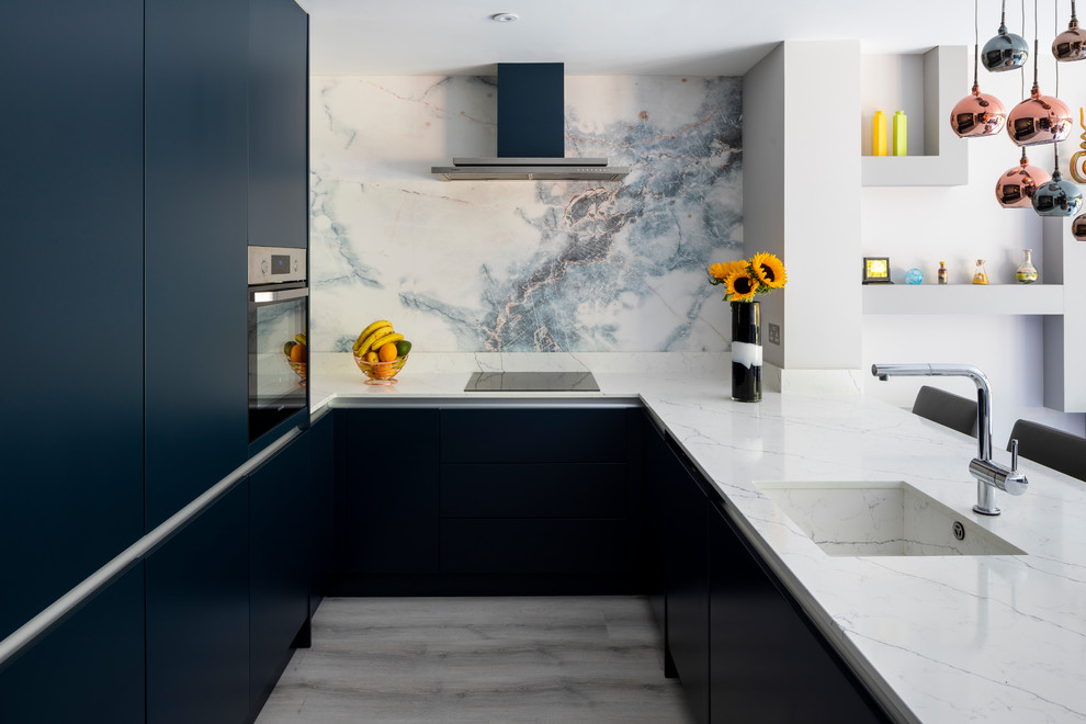 Inspiration for a mid-sized contemporary u-shaped kitchen in London with an undermount sink, flat-panel cabinets, blue cabinets, marble benchtops, white splashback, marble splashback, stainless steel appliances, no island, grey floor and white benchtop.