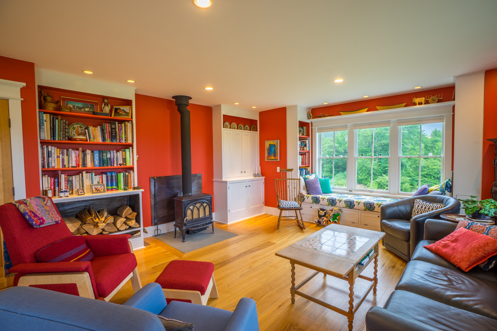 Photo of a country living room in Burlington with red walls, light hardwood floors, a wood stove and a stone fireplace surround.