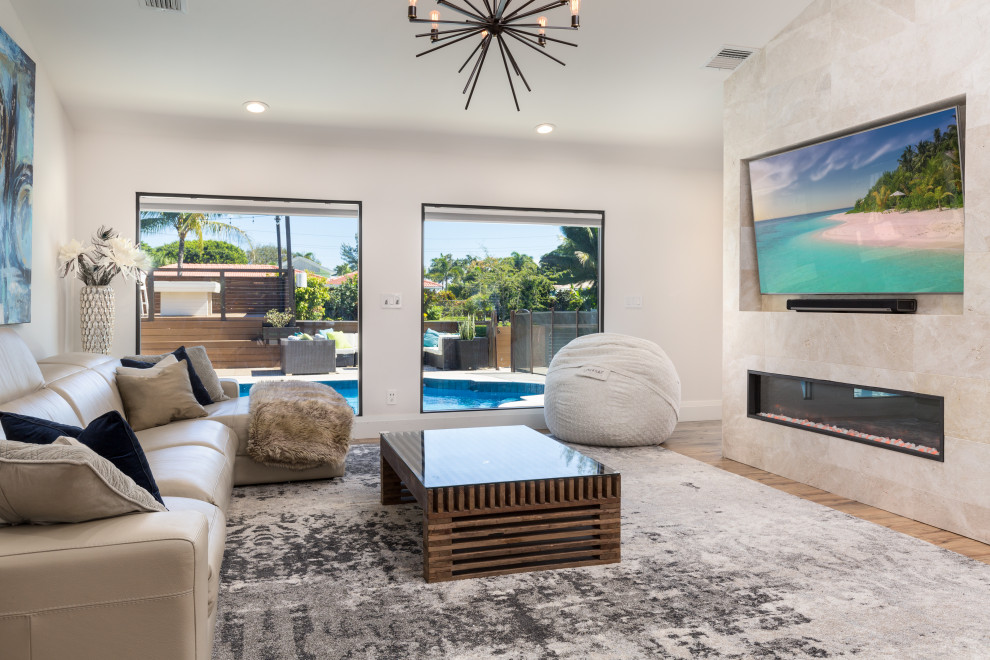 This is an example of a large contemporary open plan living room in Miami with light hardwood flooring, a standard fireplace, a stone fireplace surround and a vaulted ceiling.