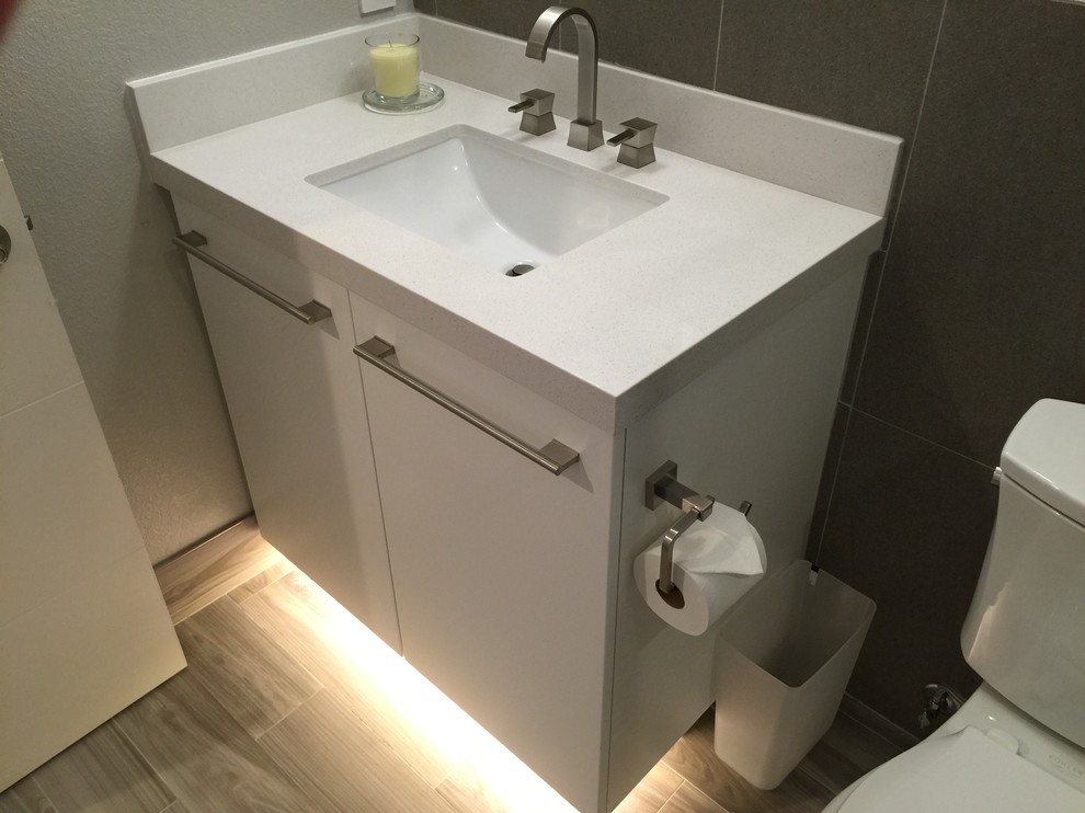 This is an example of a mid-sized contemporary powder room in San Francisco with flat-panel cabinets, white cabinets, beige walls, porcelain floors, an undermount sink and granite benchtops.