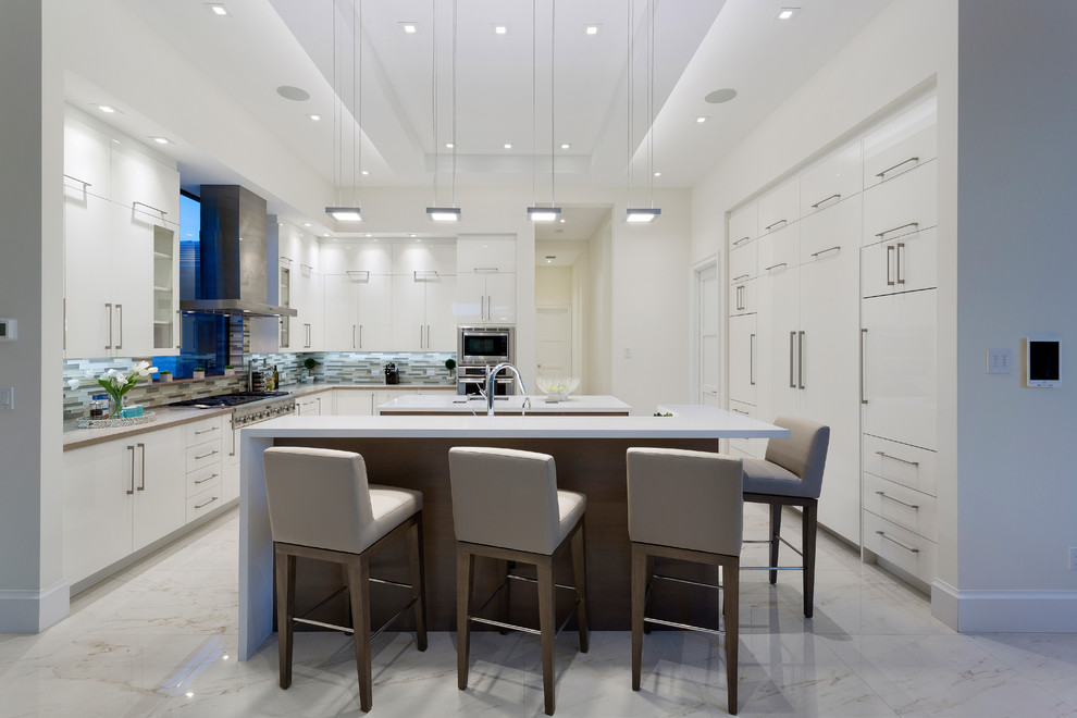 Design ideas for a large contemporary u-shaped eat-in kitchen in Miami with flat-panel cabinets, white cabinets, quartz benchtops, beige splashback, glass tile splashback, white appliances, porcelain floors, multiple islands, white floor and white benchtop.
