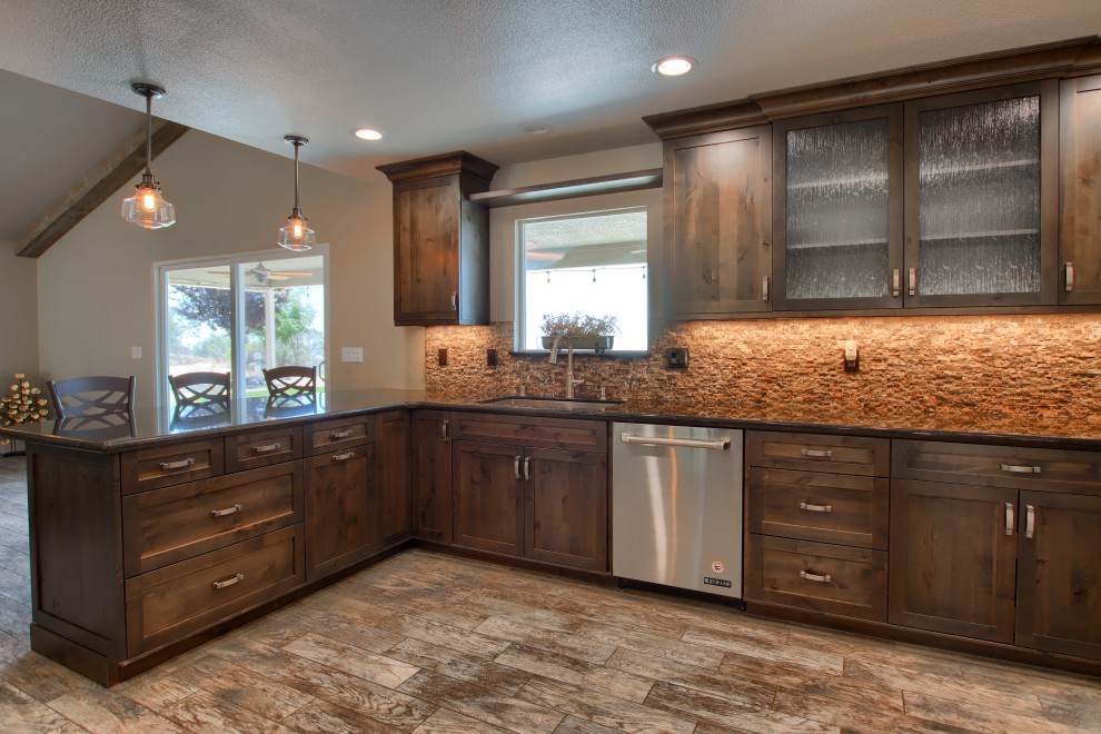 Open concept kitchen - large rustic l-shaped porcelain tile, brown floor and vaulted ceiling open concept kitchen idea with an undermount sink, shaker cabinets, brown cabinets, granite countertops, brown backsplash, marble backsplash, stainless steel appliances, an island and black countertops