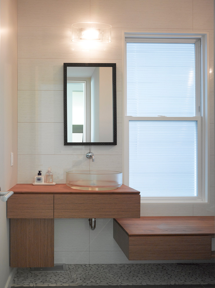 This is an example of a mid-sized modern master bathroom in San Francisco with flat-panel cabinets, medium wood cabinets, beige walls, pebble tile floors, a vessel sink, wood benchtops, grey floor and brown benchtops.