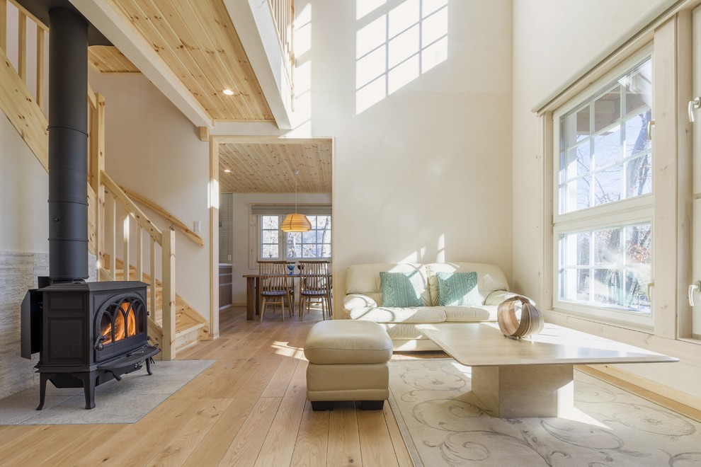 This is an example of a scandinavian living room in Other with white walls, light hardwood floors, a wood stove and no tv.