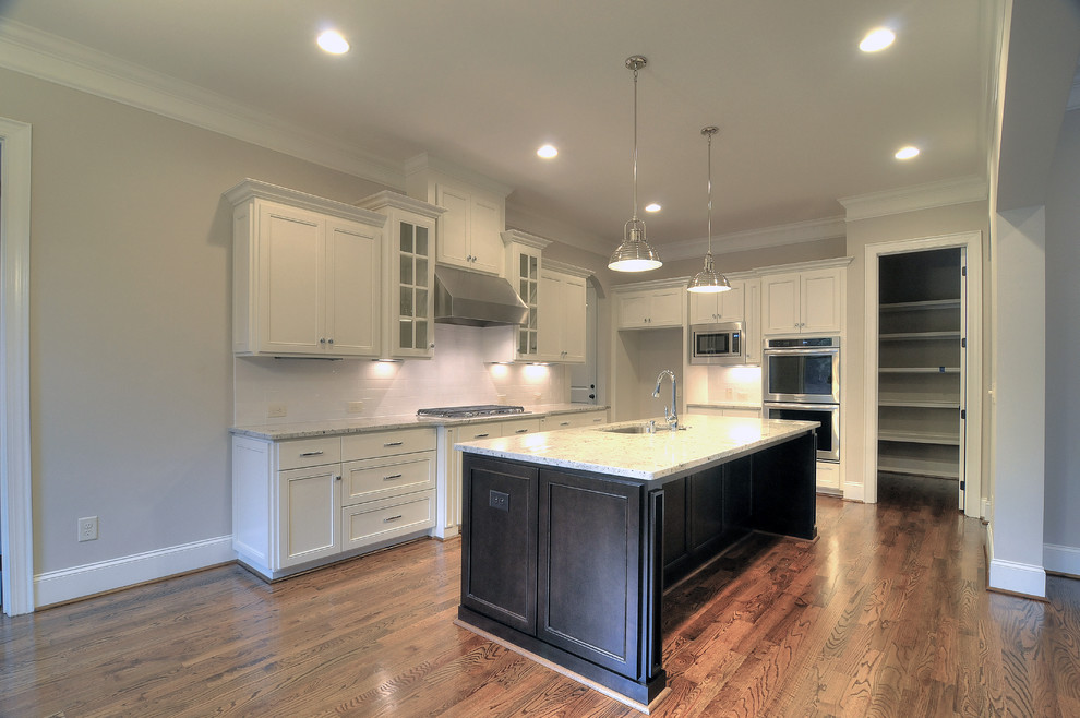 Large transitional l-shaped medium tone wood floor open concept kitchen photo in Charlotte with an undermount sink, recessed-panel cabinets, white cabinets, granite countertops, white backsplash, subway tile backsplash, stainless steel appliances and an island