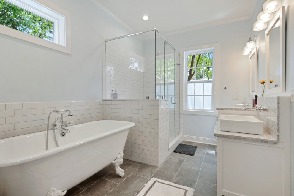 This is an example of a medium sized beach style ensuite bathroom in New Orleans with shaker cabinets, white cabinets, a claw-foot bath, a corner shower, a one-piece toilet, white tiles, metro tiles, blue walls, porcelain flooring, a vessel sink, marble worktops, grey floors, a hinged door, grey worktops, an enclosed toilet, double sinks and a freestanding vanity unit.