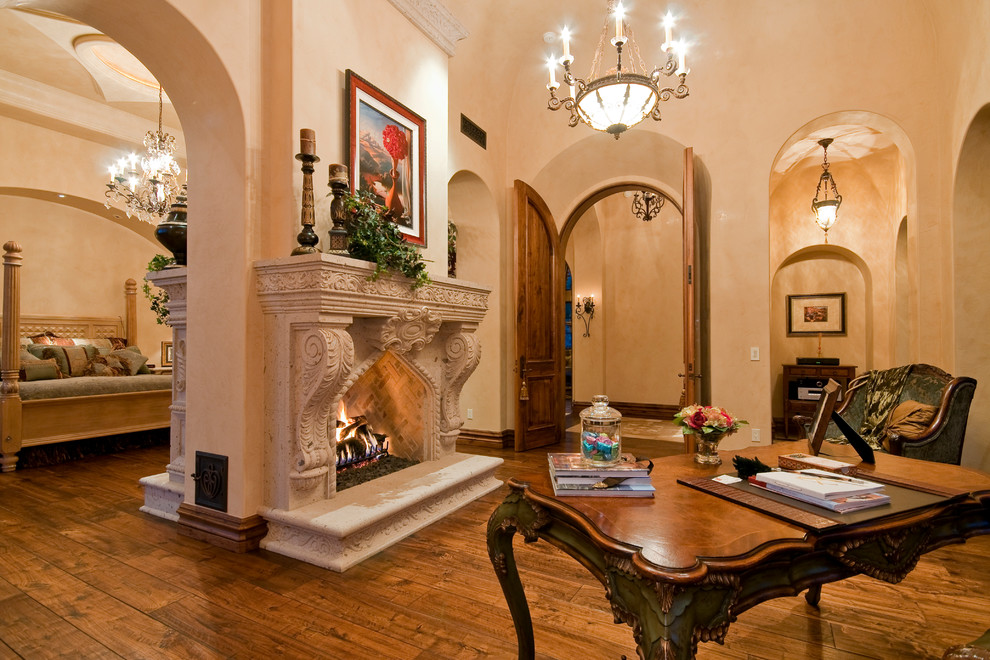 This is an example of an expansive traditional study room in Phoenix with beige walls, medium hardwood floors, a two-sided fireplace, a stone fireplace surround and a freestanding desk.