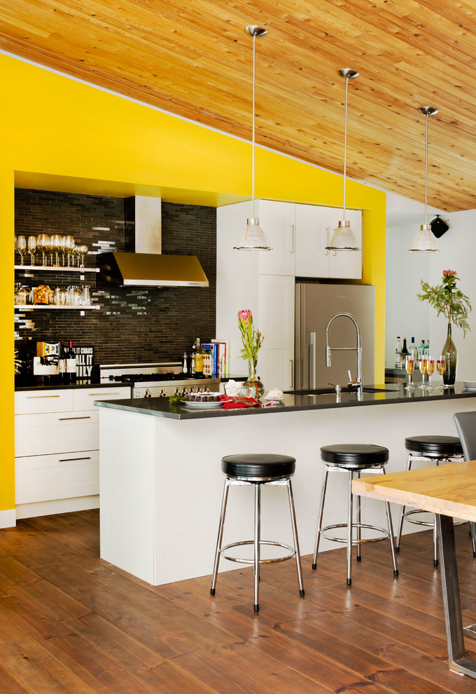 This is an example of a contemporary eat-in kitchen in Montreal with an undermount sink, flat-panel cabinets, white cabinets, black splashback, glass tile splashback and stainless steel appliances.