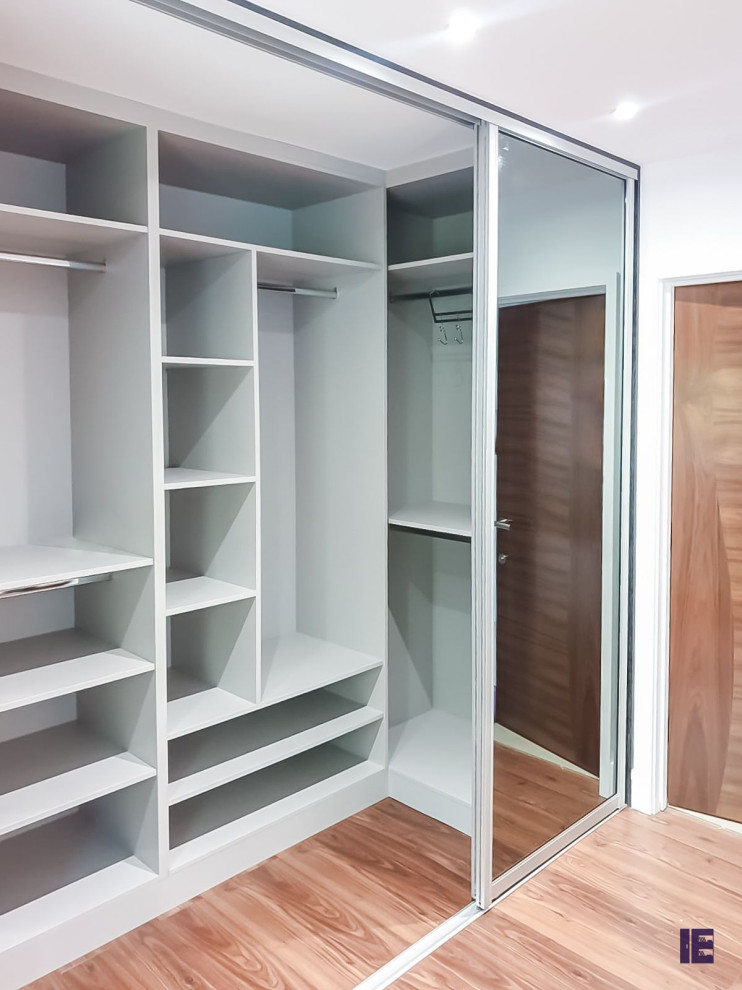 This is an example of a large modern walk-in wardrobe in London with glass-front cabinets and white cabinets.
