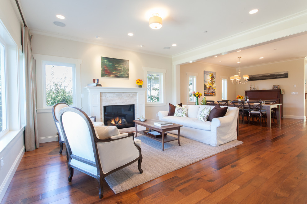 This is an example of a transitional open concept living room in Vancouver with beige walls, a standard fireplace and medium hardwood floors.