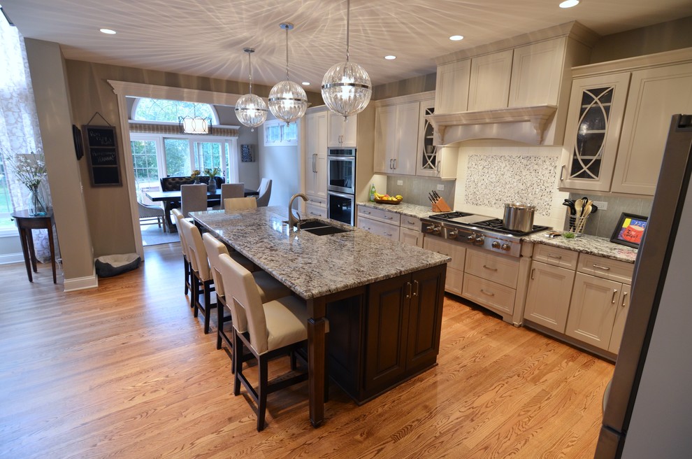 Open concept kitchen - large transitional l-shaped medium tone wood floor open concept kitchen idea in Chicago with an undermount sink, recessed-panel cabinets, white cabinets, granite countertops, gray backsplash, porcelain backsplash, stainless steel appliances and an island