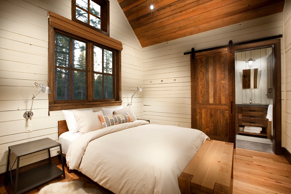 Country guest bedroom with white walls, medium hardwood floors and brown floor.
