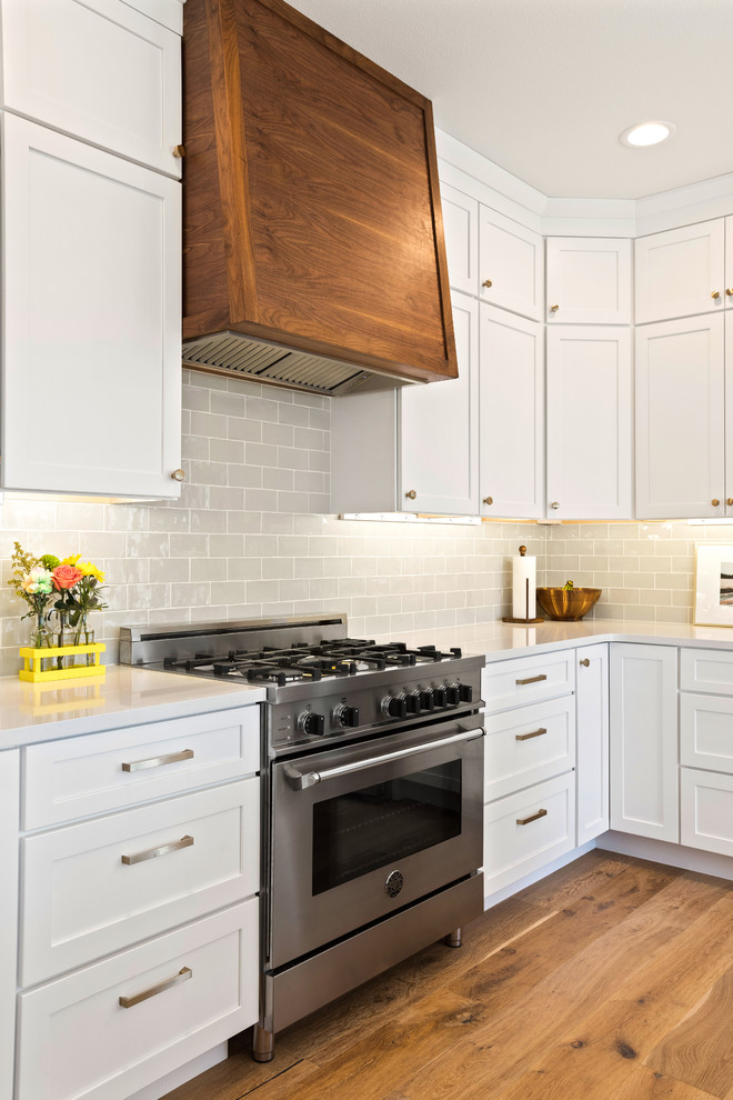 Inspiration for a transitional l-shaped light wood floor and brown floor kitchen remodel with a farmhouse sink, shaker cabinets, white cabinets, quartz countertops, white backsplash, subway tile backsplash, stainless steel appliances, an island and white countertops