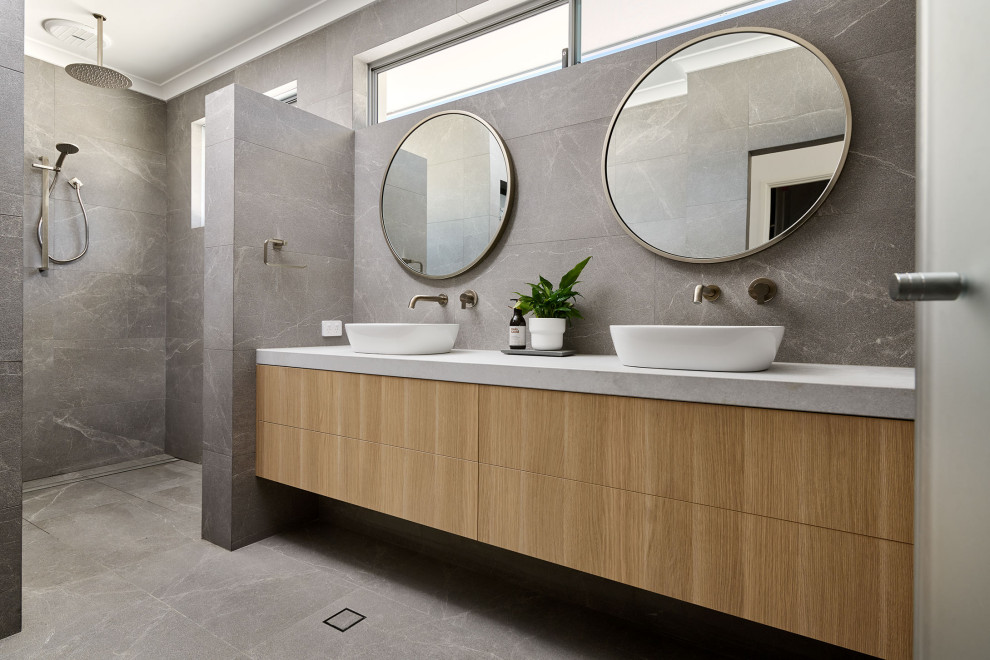 Photo of a mid-sized master bathroom in Perth with furniture-like cabinets, light wood cabinets, an open shower, a one-piece toilet, gray tile, ceramic tile, white walls, ceramic floors, a vessel sink, engineered quartz benchtops, grey floor, an open shower, grey benchtops, an enclosed toilet, a double vanity and a floating vanity.