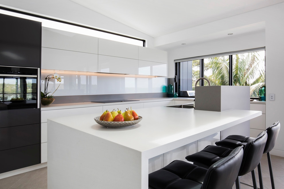 Inspiration for a contemporary l-shaped kitchen in Sydney with a double-bowl sink, flat-panel cabinets, white splashback, black appliances, concrete floors, with island, grey floor and white benchtop.