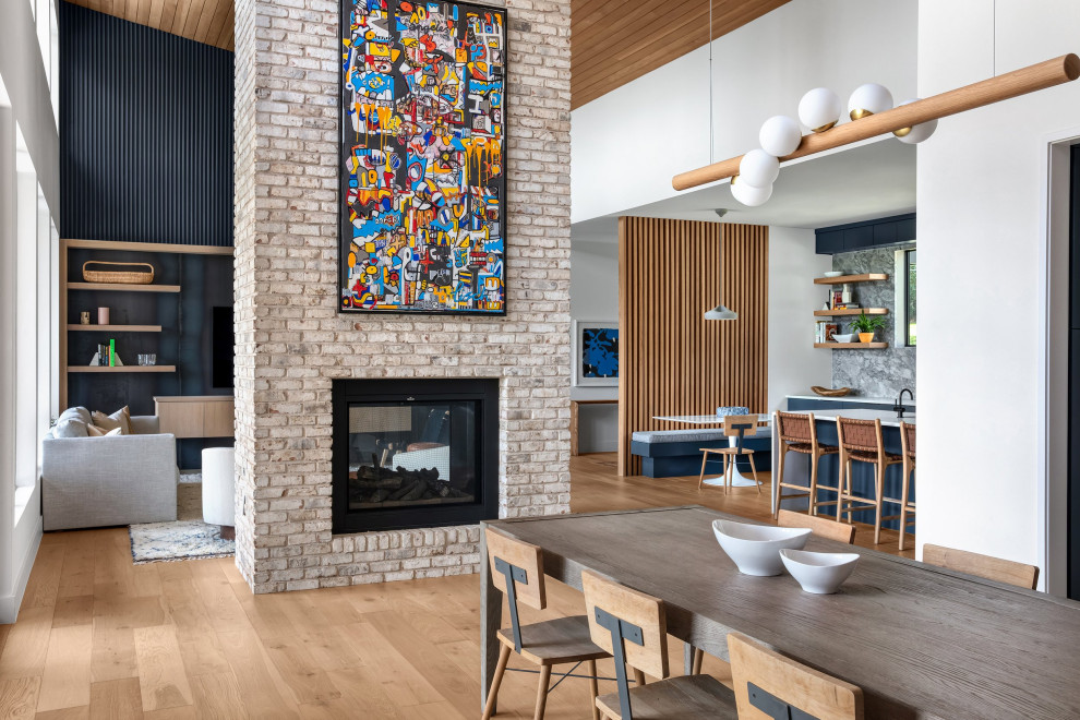 Cette photo montre une grande salle à manger ouverte sur le salon rétro avec parquet clair, une cheminée double-face, un manteau de cheminée en brique et un plafond en bois.