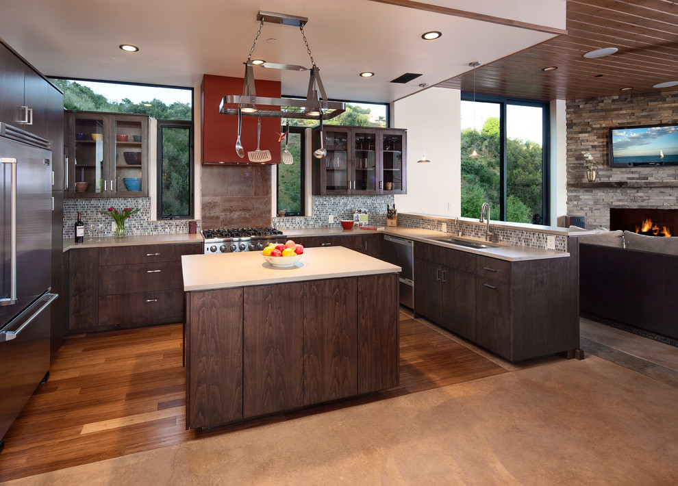 Mid-sized contemporary u-shaped open plan kitchen in Santa Barbara with an undermount sink, glass-front cabinets, dark wood cabinets, solid surface benchtops, multi-coloured splashback, stainless steel appliances, medium hardwood floors, with island, mosaic tile splashback and orange floor.
