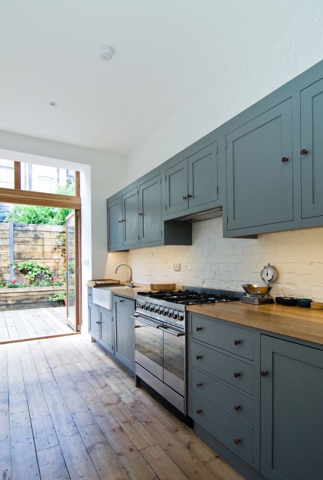 Design ideas for a mid-sized contemporary single-wall eat-in kitchen in London with wood benchtops, white splashback, medium hardwood floors, a farmhouse sink and blue cabinets.
