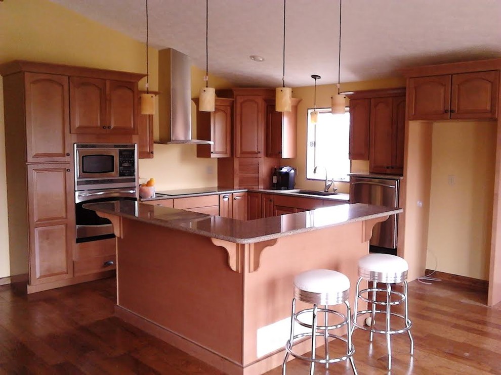 Bild på ett kök, med en nedsänkt diskho, luckor med lamellpanel, skåp i mellenmörkt trä, rostfria vitvaror och mellanmörkt trägolv