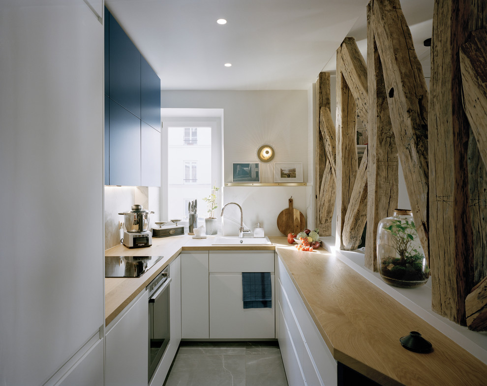Inspiration for a small contemporary u-shaped open plan kitchen in Paris with an integrated sink, beaded inset cabinets, blue cabinets, wood benchtops, white splashback, marble splashback, stainless steel appliances, ceramic floors, no island, grey floor and brown benchtop.