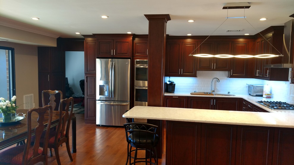 Inspiration for a large transitional u-shaped medium tone wood floor kitchen remodel in New York with an undermount sink, raised-panel cabinets, dark wood cabinets, white backsplash, subway tile backsplash, stainless steel appliances and a peninsula